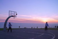 two men playing basketball on a court in front of the ocean