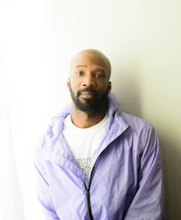 a man in a purple jacket leaning against a wall